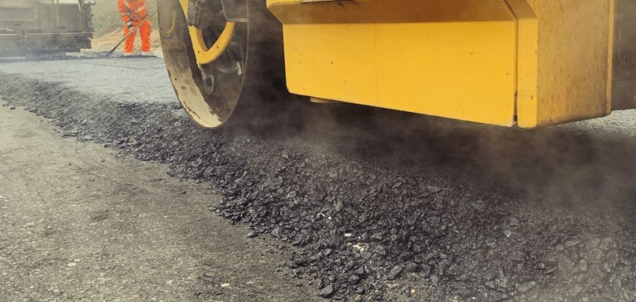 Asphalt wird auf Straße aufgebracht und gewalzt.