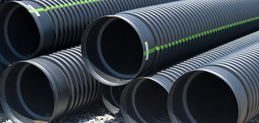 Mehrere Drainage-Rohre liegen übereinandergestapelt auf einem Platz.