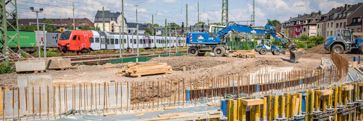 In den kommenden Monaten entsteht zwischen den Koblenzer Stadtteilen Rauental und Goldgrube eine neue Fuß- und Radwegebrücke. Ein Bagger steht an einer Baugrube. Im Hintergrund sind Bahngleise zu sehen.