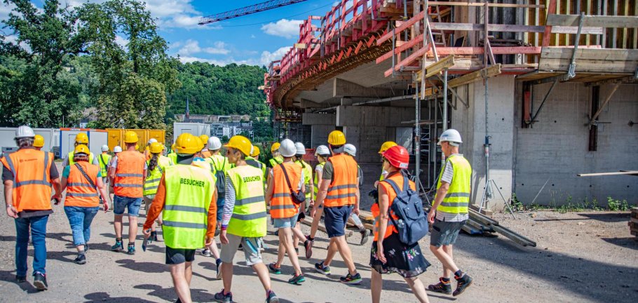 Eine Besuchergruppe in Warnwesten läuft über eine Baustelle. Eine Besuchergruppe in Warnwesten läuft über eine Baustelle.