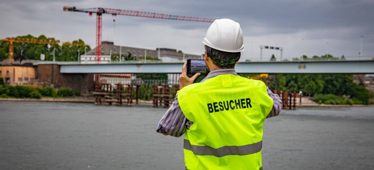 Ein Mann, der eine Weste mit dem Aufdruck Besucher trägt, fotografiert eine Brücke.