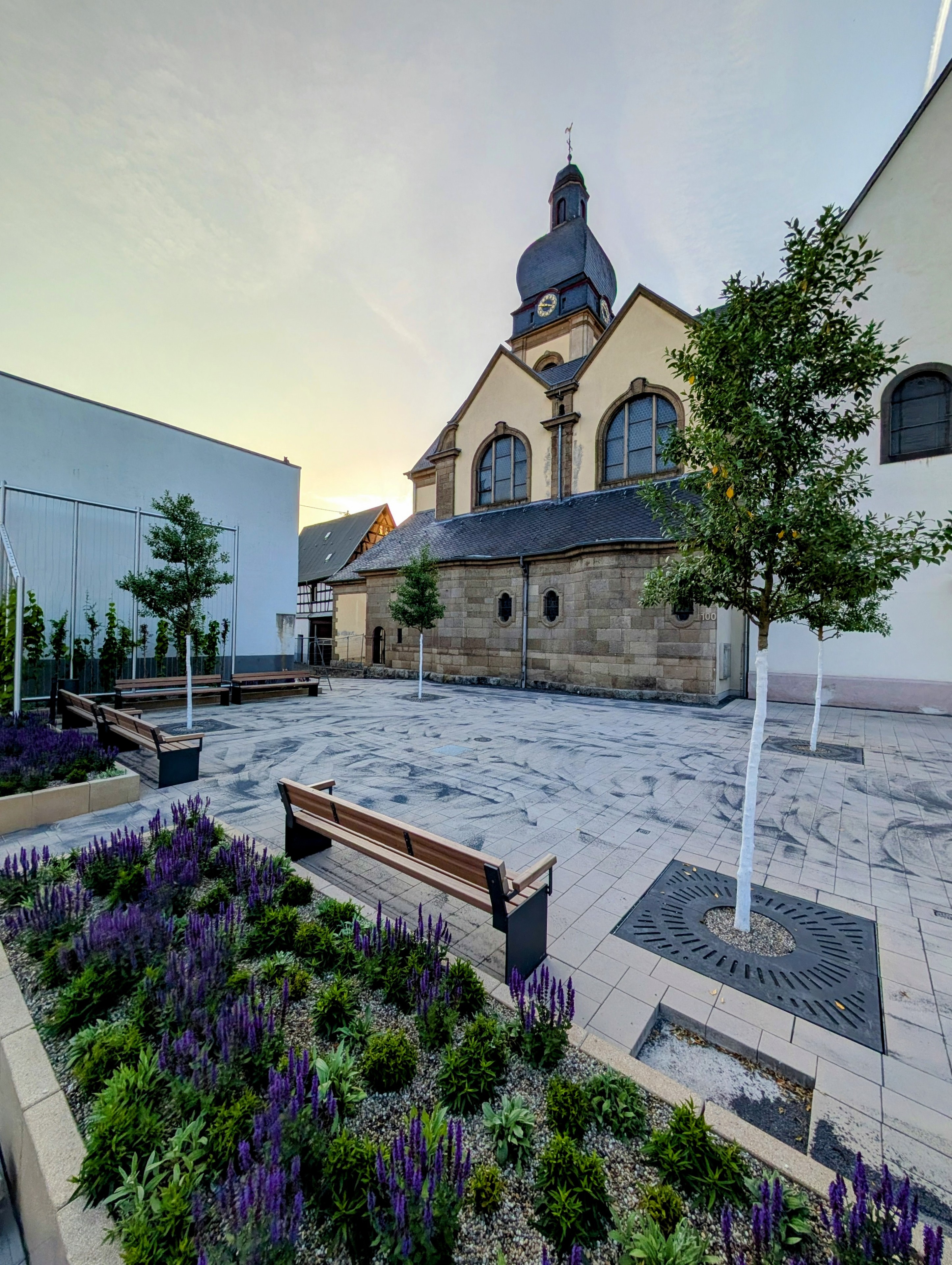 Ein neu angelegter Platz, im Vordergrund Blumenbeete. Im Hintergrund eine Kirche.