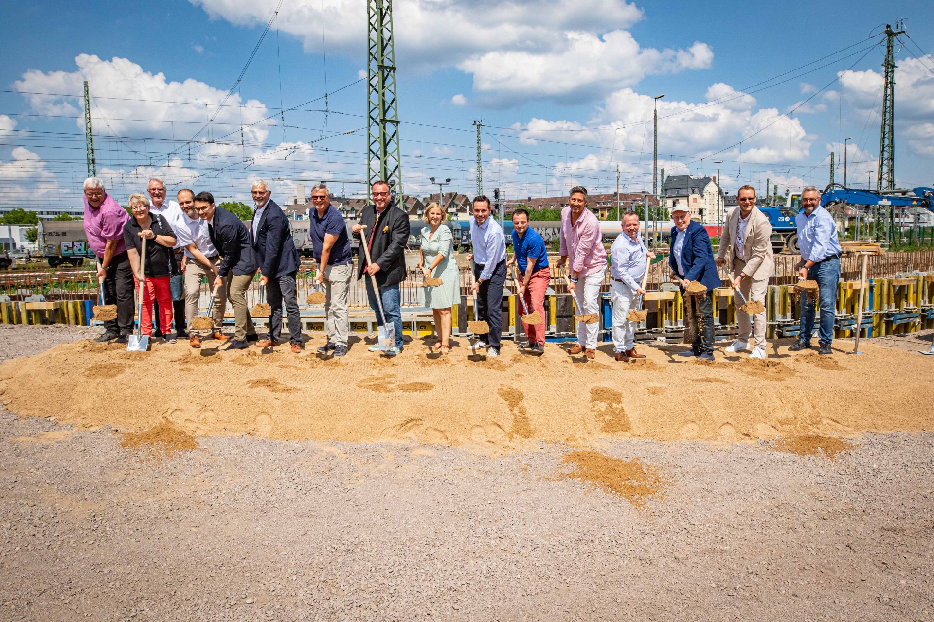 Beim Spatenstisch für die neue Fuß- und Radwegebrücke zwischen den Koblenzer Stadtteilen Goldgrube und Rauental waren neben Vertretern aus Politik und der beteiligten Unternehmen auch (ab 8. von links) Verkehrsstaatssekretär Andy Becht, Mobilitätsministerin Katrin Eder, Oberbürgermeister David Langner und Baudezernent Prof. Dr. Andreas Lukas dabei. Mehrere Menschen stehen in einer Reihe und werfen mit Spaten Sand in die Luft.