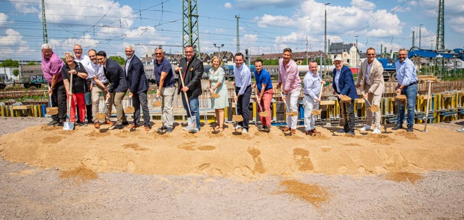 Beim Spatenstisch für die neue Fuß- und Radwegebrücke zwischen den Koblenzer Stadtteilen Goldgrube und Rauental waren neben Vertretern aus Politik und der beteiligten Unternehmen auch (ab 8. von links) Verkehrsstaatssekretär Andy Becht, Mobilitätsministerin Katrin Eder, Oberbürgermeister David Langner und Baudezernent Prof. Dr. Andreas Lukas dabei. Mehrere Menschen stehen in einer Reihe und werfen mit Spaten Sand in die Luft.