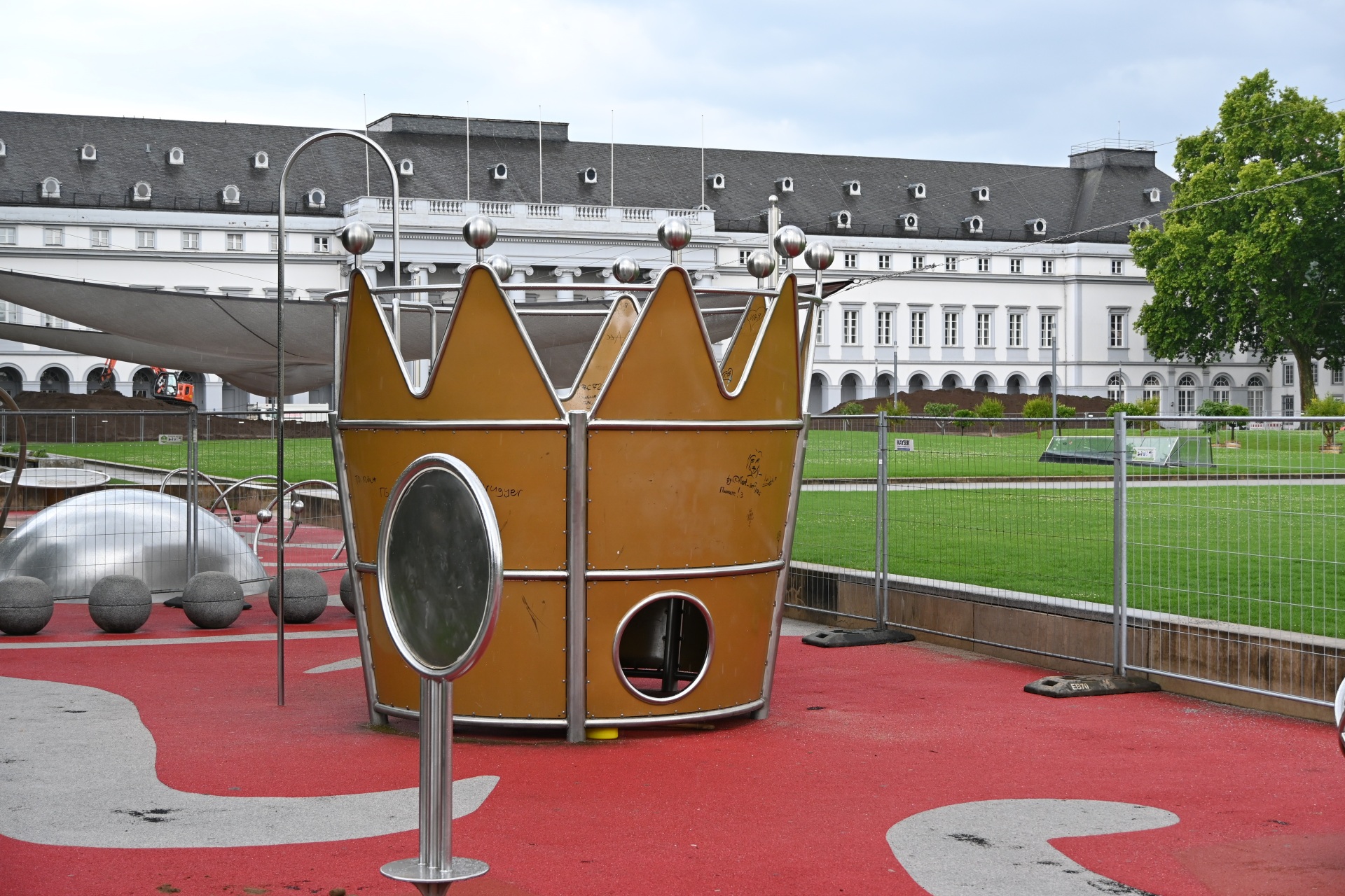 Eine überdimensionale Krone steht auf einem Spielplatz. Der Spielplatz ist mit Bauzäunen umstellt.