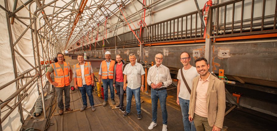 Gemeinsam mit Vertretern des städtischen Tiefbauamtes, der Koblenzer Politik und Pressvertretern sah sich der Koblenzer Oberbürgermeister David Langner (rechts) den aktuellen Stand des Neubau des Rad- und Gehweges an der Horchheimer Eisenbahnbrücke an. Mehrere Menschen stehen in einer Reihe auf einer Baustelle.