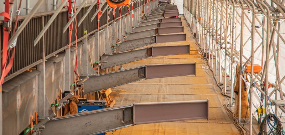 Bereits jetzt ist an der Horchheimer Eisenbahnbrücke gut zu erkennen, dass der zukünftige Rad- und Fußweg über den Rhein deutlich breiter wird als zuletzt. Mehrere Stahlbauteile ragen auf einer Baustelle in den Raum hinein.