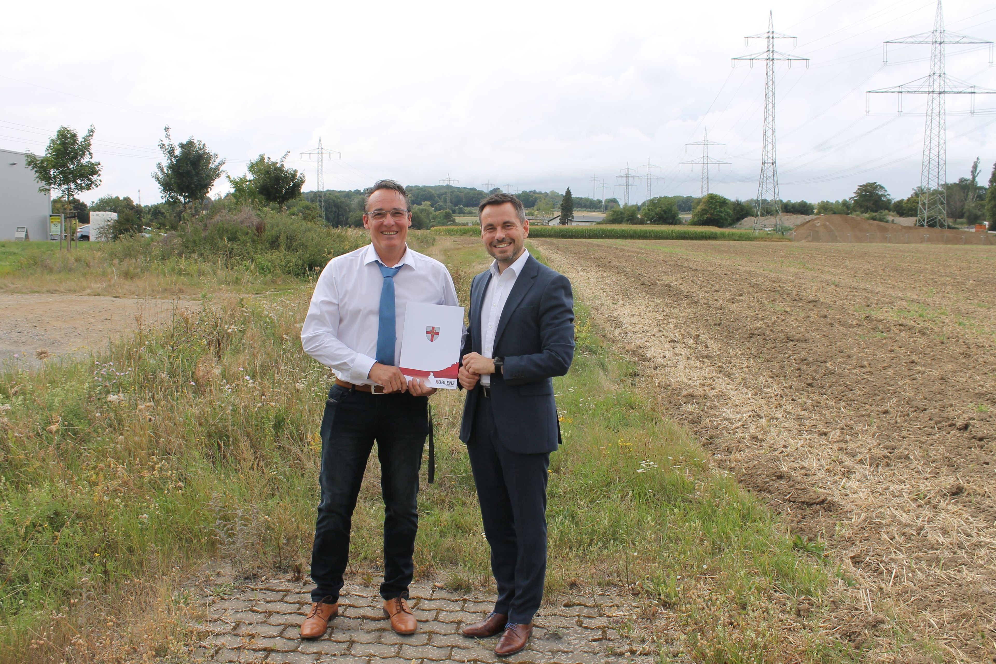 2 Männer stehen an einem Endstück eines Weges. Im Hintergrund Felder.