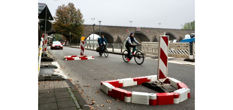 Eine rot-weiße Fahrbahneinengung an der Radfahrer vorbeifahren. Im Hintergrund nähert sich ein Auto.