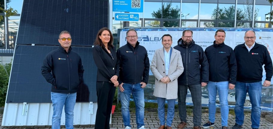 Personen stehen auf einem Parkplatz. Im Hintergrund eine verglaste Gebäudefassade.