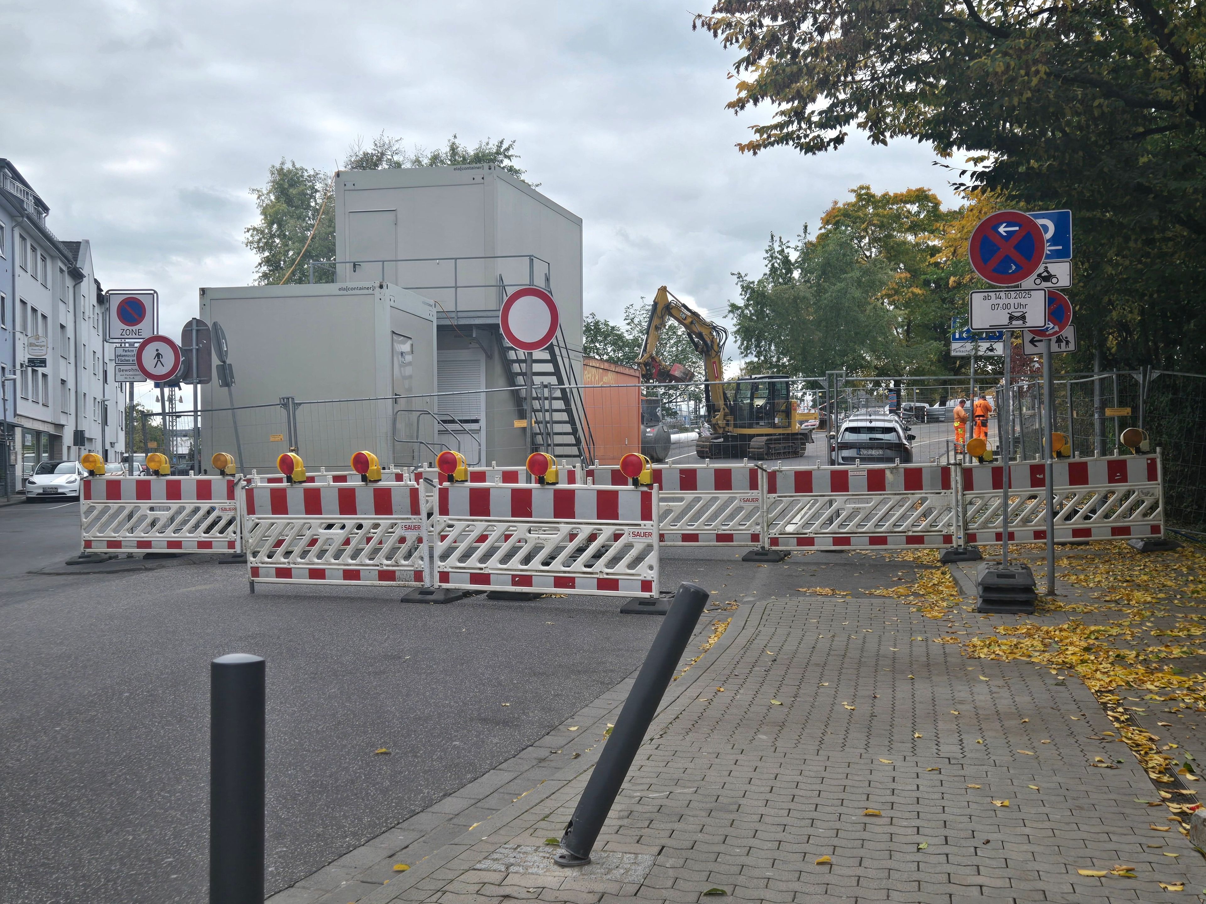Eine abgesperrte Baustelle mit Containern und einem Bagger im Hintergrund.