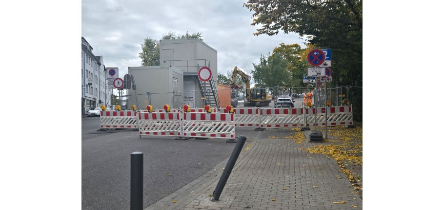 Eine abgesperrte Baustelle mit Containern und einem Bagger im Hintergrund.