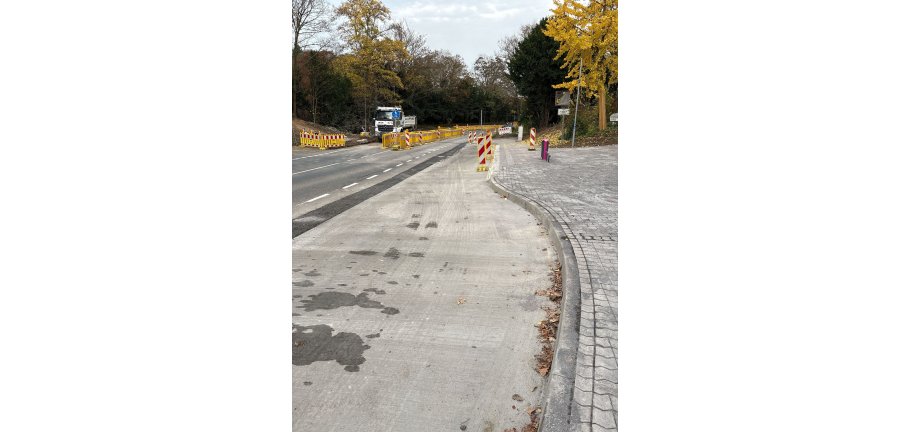 Eine Baustelle mit Absperrungen für den Fahrzeugverkehr. Außerdem ist eine fertiggestellte Bushaltestelle zu sehen.