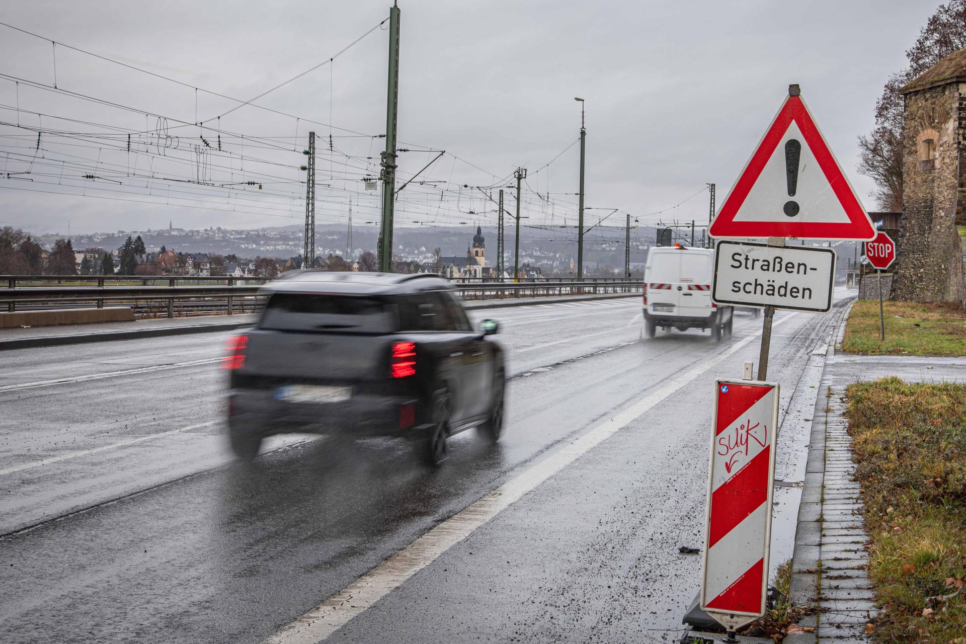 Ein Auto fährt auf einer Straße an einem Schild vorbei. Auf dem Schild steht Straßenschäden als Aufschrift.