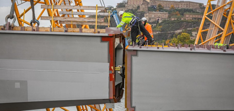 Zwei Bauarbeiter stehen auf einem Stahlteil an der einer Brücke. Zwei Bauarbeiter stehen auf einem Stahlteil an der einer Brücke.