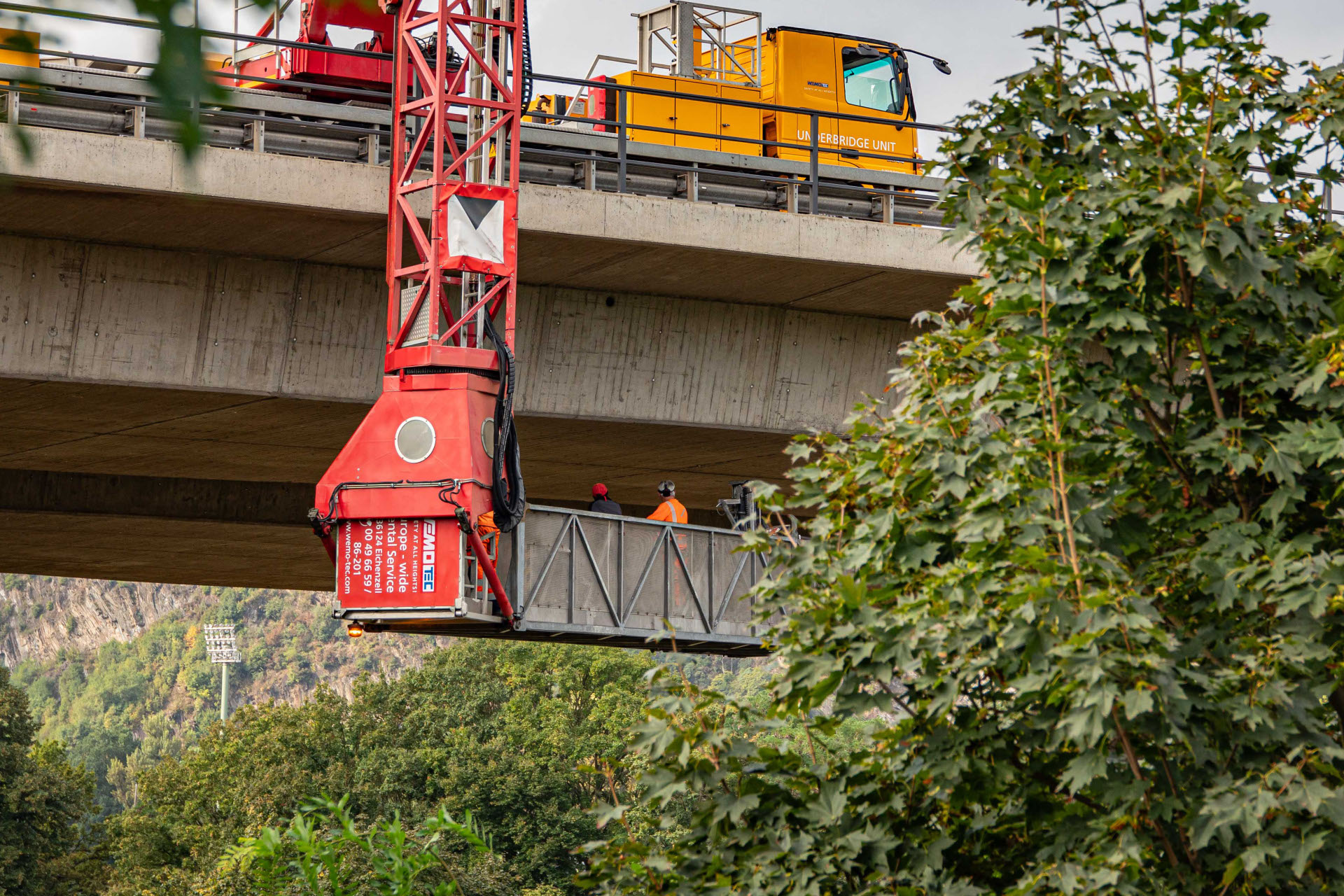 Bauarbeiter kontrollieren von einem Unterflurgerät aus eine Brücke.
