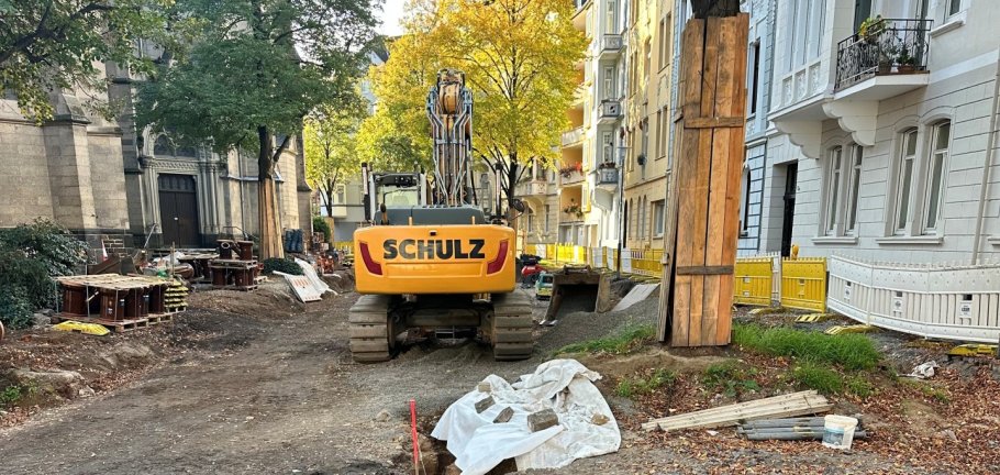 Ein Bagger steht auf einer Straßenbaustelle an einem Baum.