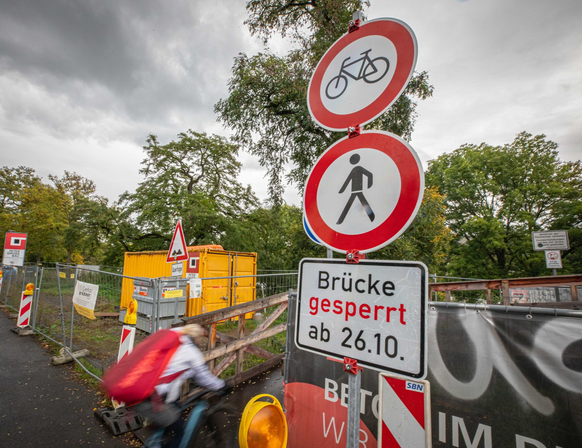 Eine Fahrradfahrerin fährt an einem Hinweisschild für eine Brückensperrung vorbei. Eine Fahrradfahrerin fährt an einem Hinweisschild für eine Brückensperrung vorbei.